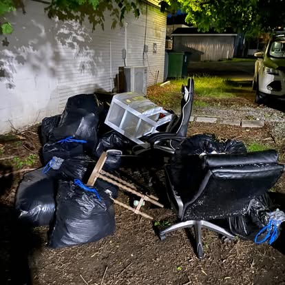 Yard piled with trash bags, a broken office chair and scrap before removal