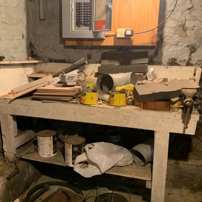 Basement workbench covered in scrap lumber, paint cans and old tools before removal