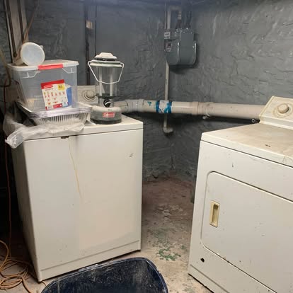 Basement corner with an old washer, dryer and storage totes before removal